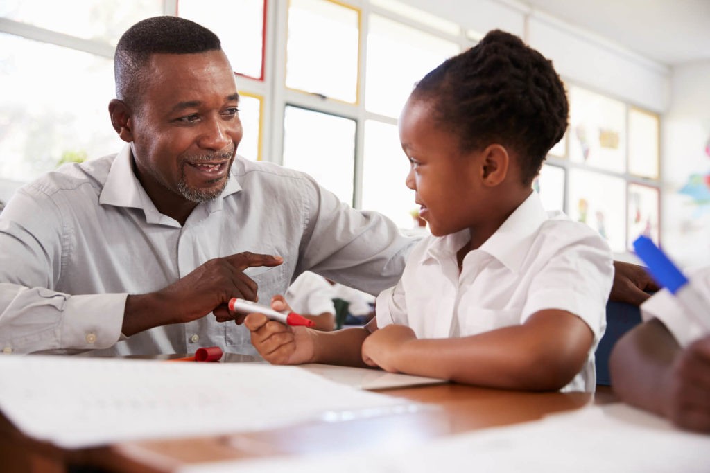 Teacher helping a young girl at her desk.