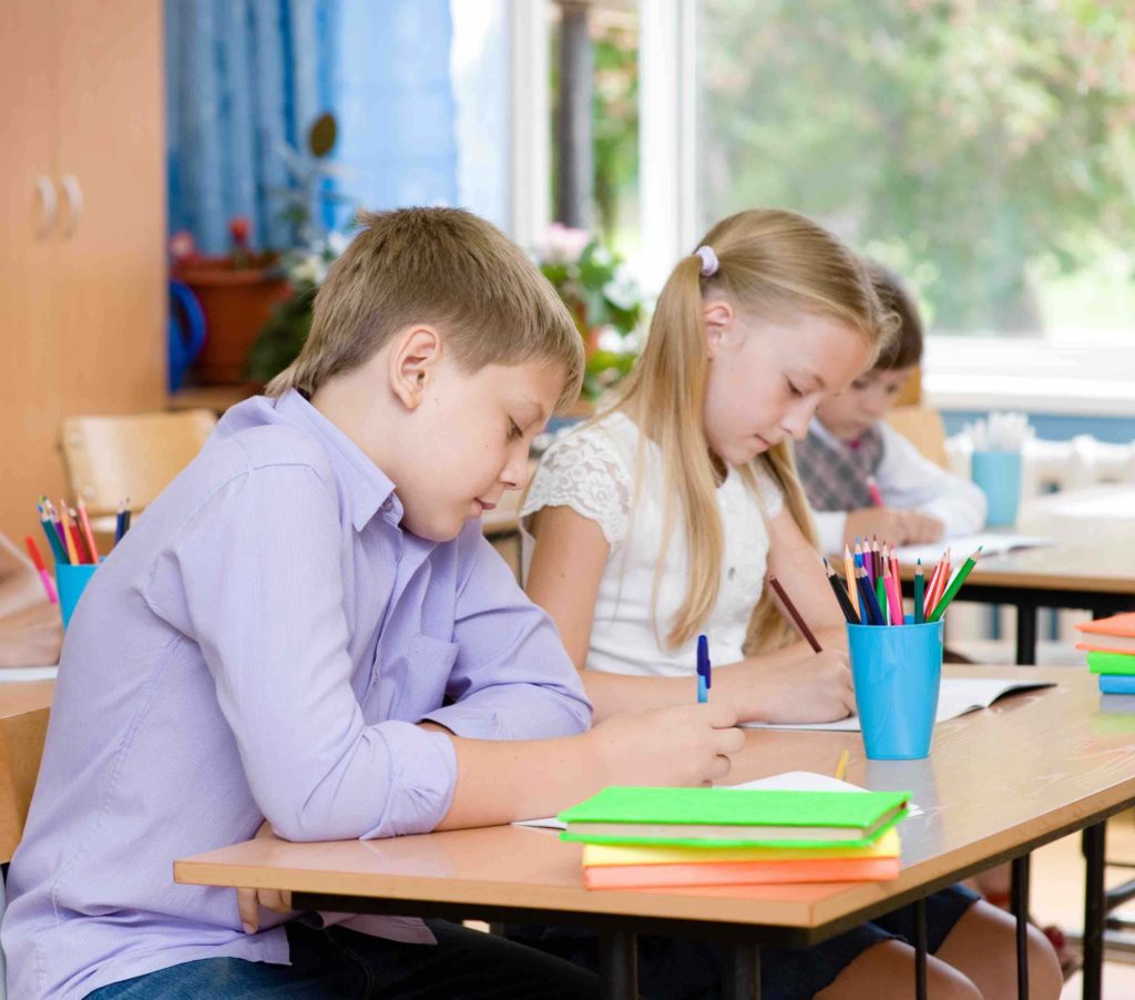 Two young students sitting at their desk writing on paper