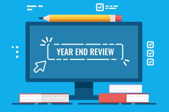 Computer screen with the words ‘Year End Review’ surrounded by books and a pencil