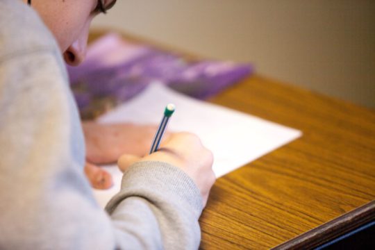 Boy sitting at a desk writing on paper.