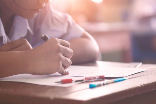 Young student writing on piece of paper at her desk