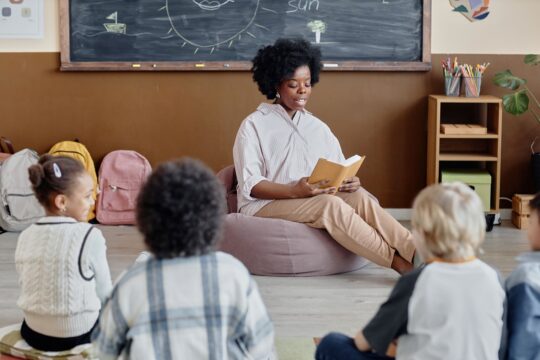 A teacher sits with her class, leading read-alouds.