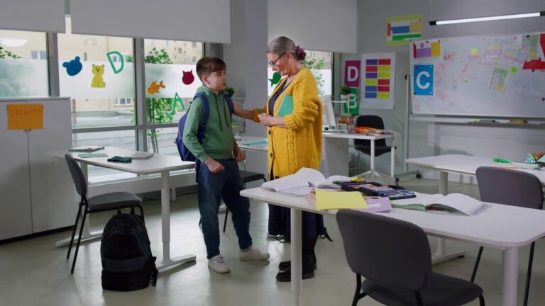 A teacher stands with her student after class, privately talking.