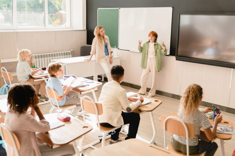 A student stands at the front of the classroom, talking to her peers and giving a student presentation.