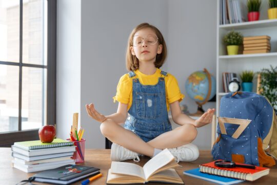 A student sits at her desk, doing meditation in a calm classroom.