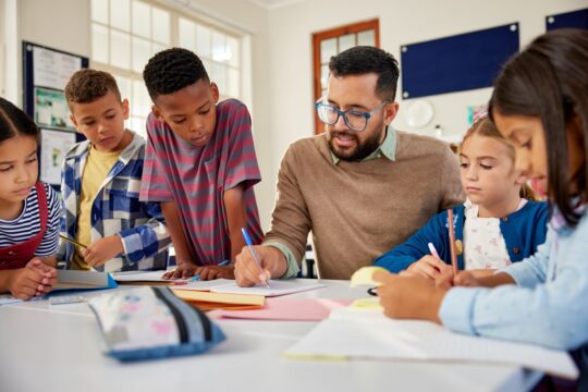 A teacher sits with his students while giving them feedback on their work.