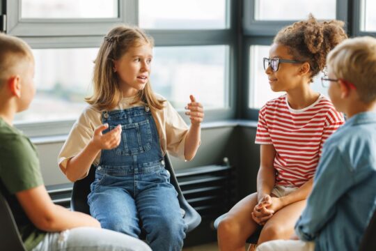 A group of students sit in a circle, having a discussion, representing think, pair, share.