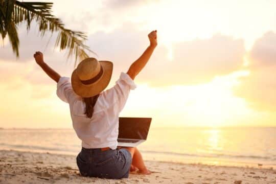 Summer PD for teachers: a woman sits on the beach with her laptop.