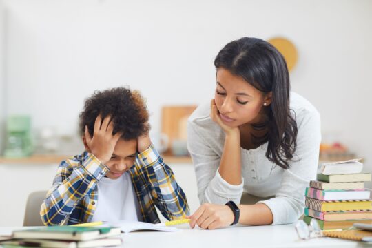 A teacher sits next to a boy with his head in his hands, representing struggling students.