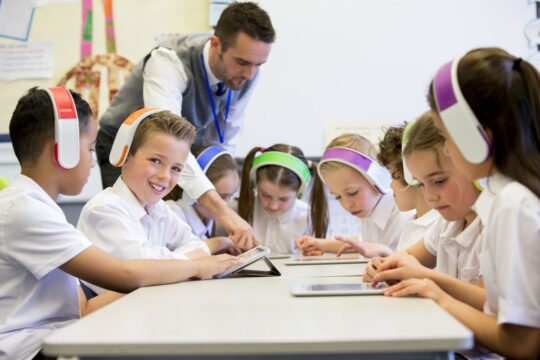 Relaxing music in the classroom: students sit around a table, listening to music in their headphones as they work on their iPads.
