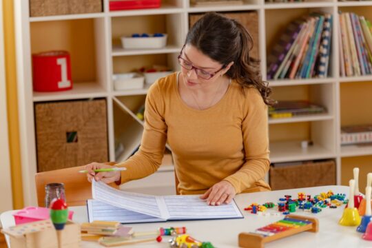 How to lesson plan for new teachers: a kindergarten teacher sits at one of the tables in her classroom and makes a lesson plan.