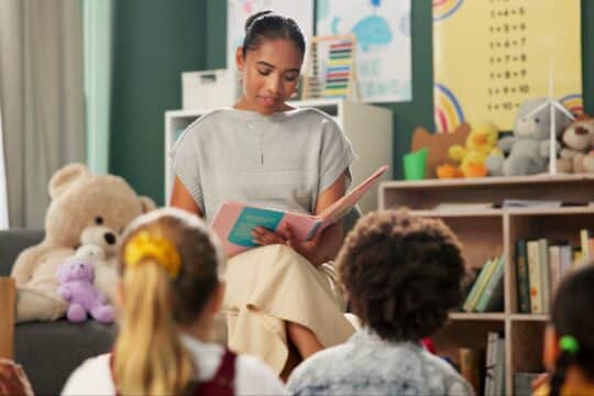 A teacher sits in front of her students, reading them a story and discussing themes in literature.
