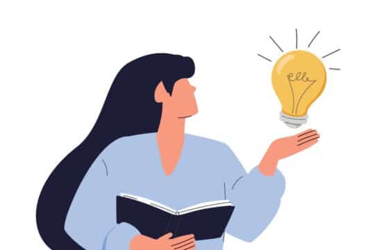 A teacher holds a book in one hand and a light bulb in the other.