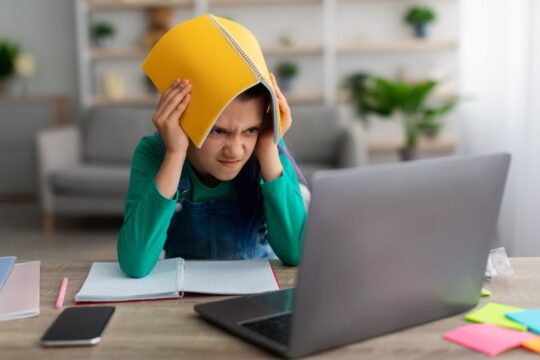 An angry student holds a book over her head in frustration, stressing over homework.