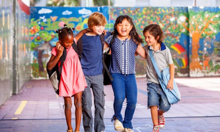 Four multi-cultural children walk through school with their arms around each other.